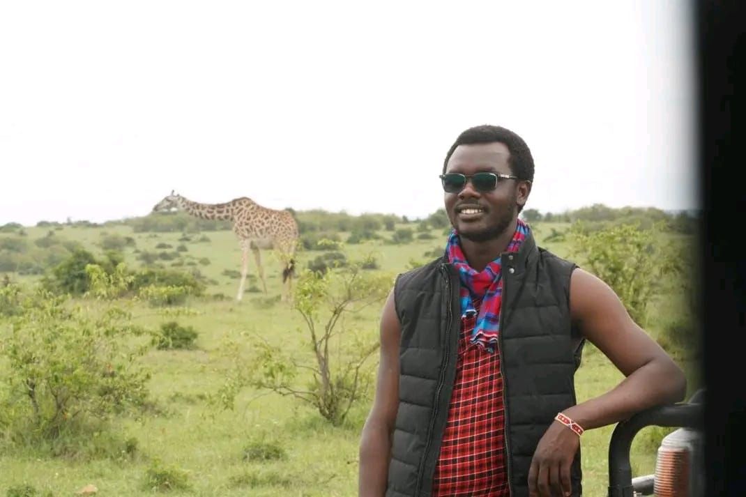 Sylvester by the vehicle with a giraffe grazing behind him